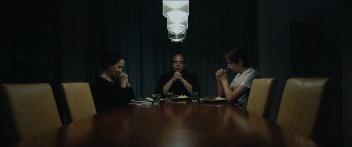 Still from the film Gesloten Deuren. The father is at the head of the table, the mother on the left and Jasper on the right. They are holding their hands in prayer.