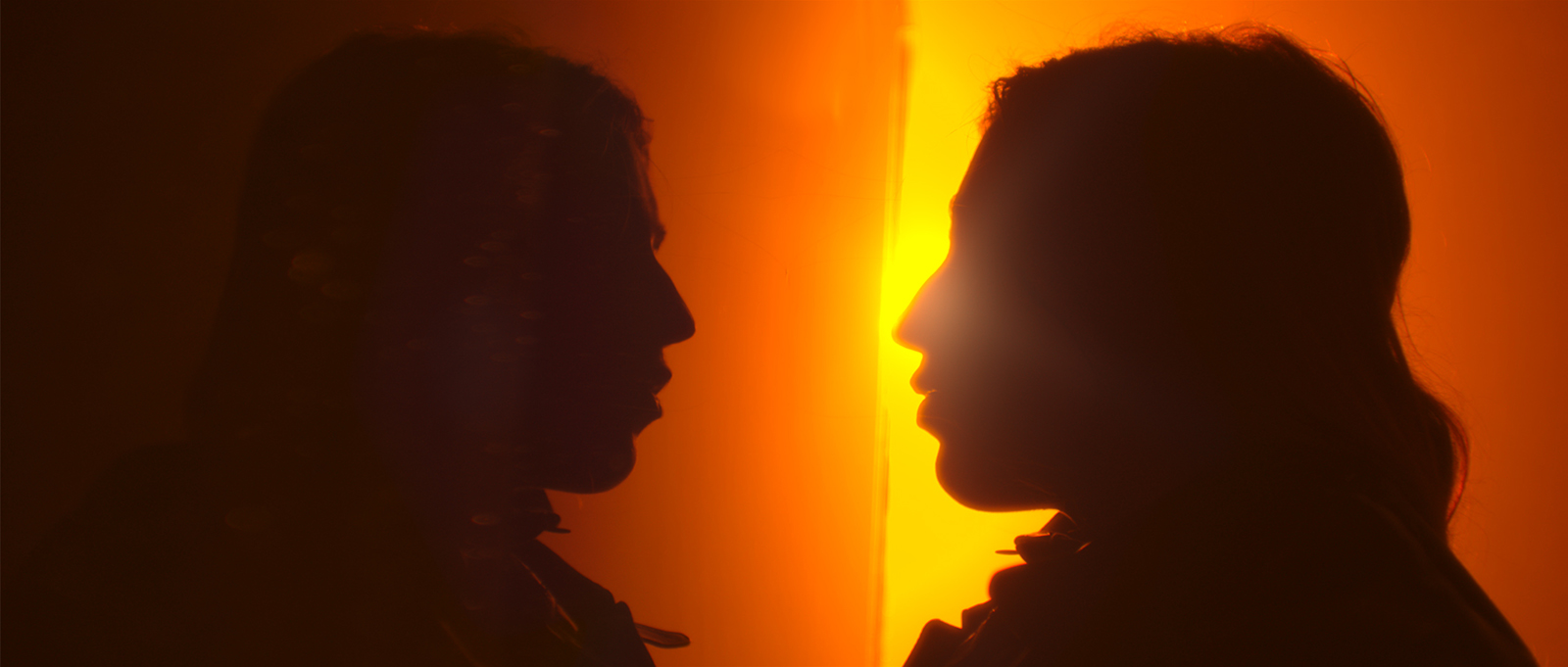 Still from the film Ningyo. Valentina is in silhouette, looking at her own reflection in a body of water. There's beautiful orange light behind her.