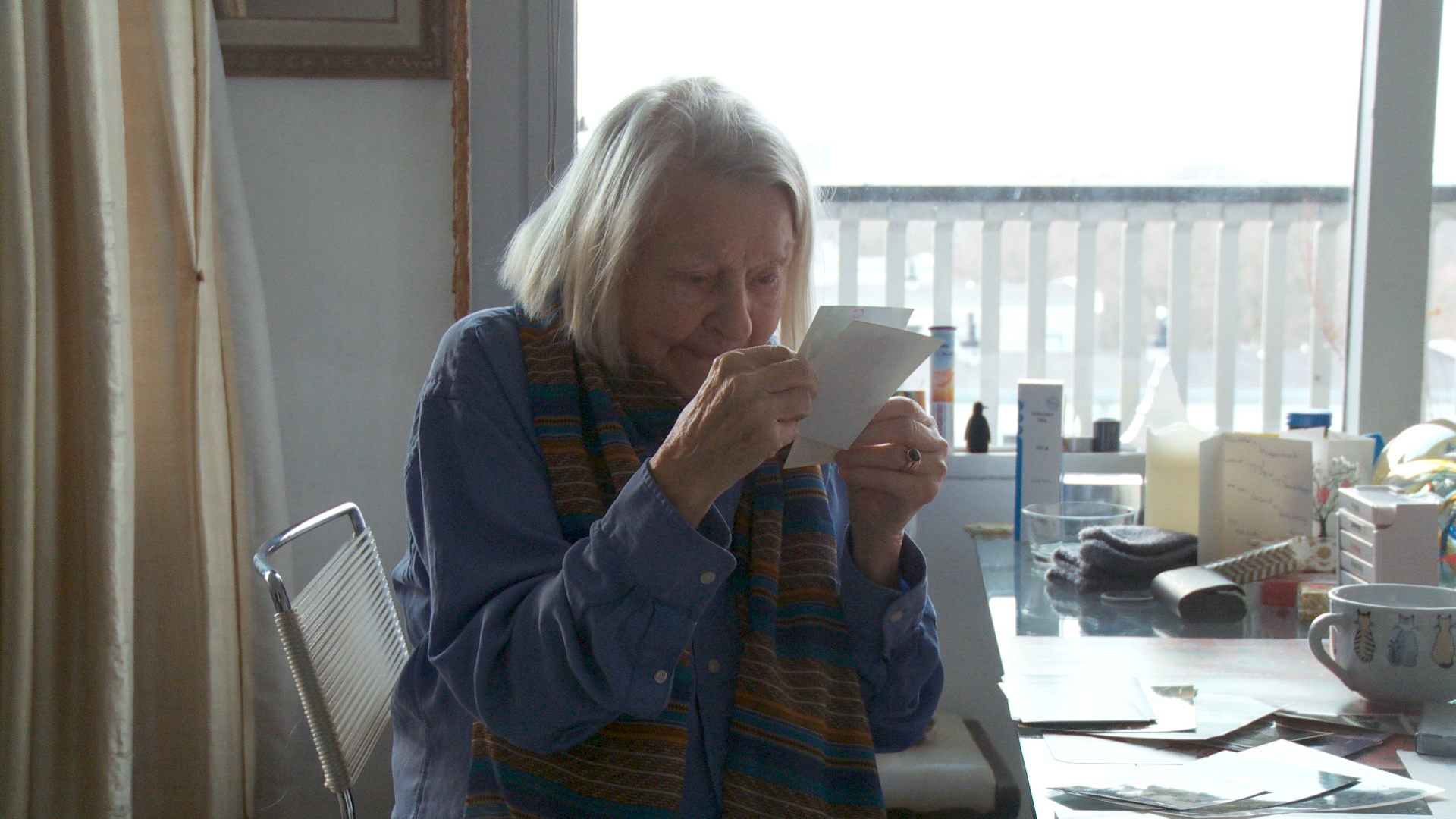 Still from the film Een klein beetje nog. Elisabeth is sitting at her dining table looking at old pictures.