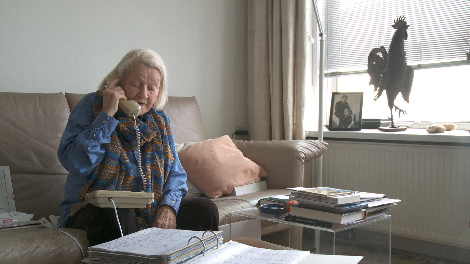 Still from the film Een klein beetje nog. Elisabeth is sitting on her couch on the phone.