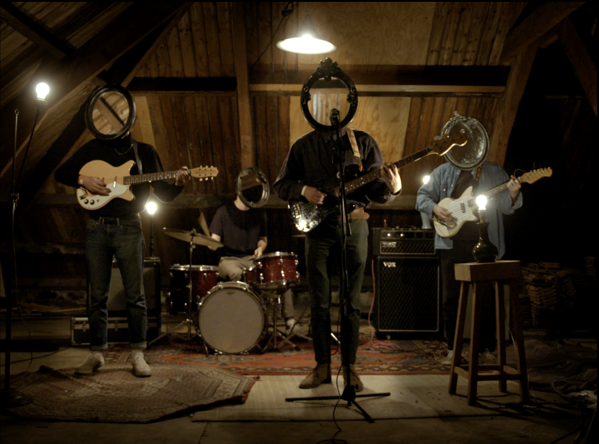 Still from the music video for The Hazzah - I'm Your Man. The band is standing in an attic performing, but their heads are all mirrors. 