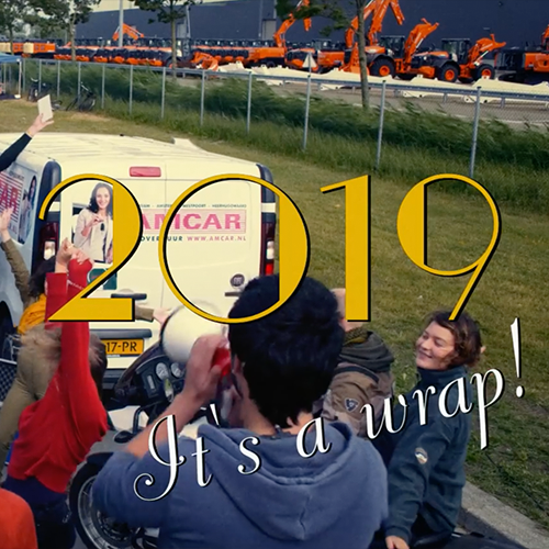Thumbnail the promo film Nieuwe Dag Op Set. There's some cars in the background and people's back turned to the camera in the foreground. There's a title that says "2019, it's a wrap!".
