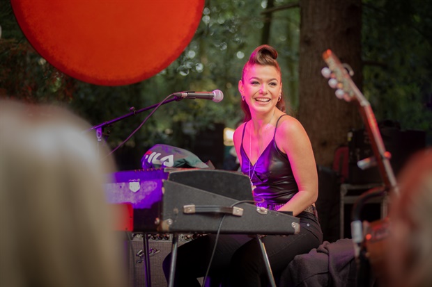 Still from Buiten is het Feest. A medium-wide shot of Sonne on the podium during a concert. She's sitting behind a piano and smiling.
