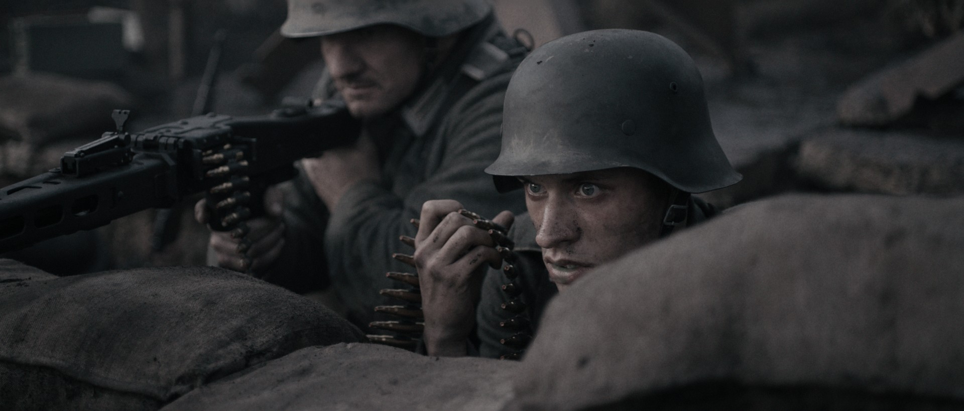 Still from the film De Slag om de Schelde/The Forgotten Battle. Marinus is crouched down in the front lines of a battle field, holding the ammo for a rifle next to him.