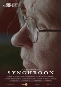 Poster for the film 'Synchroon'. It shows a close-up of an old woman in profile. She's looking to the left of the poster, the background is a dark green. She's wearing glasses and looks a bit sad. On the bottom are the film's title and credits. In the upper left corner is the logo for GoShort International Film Festival.