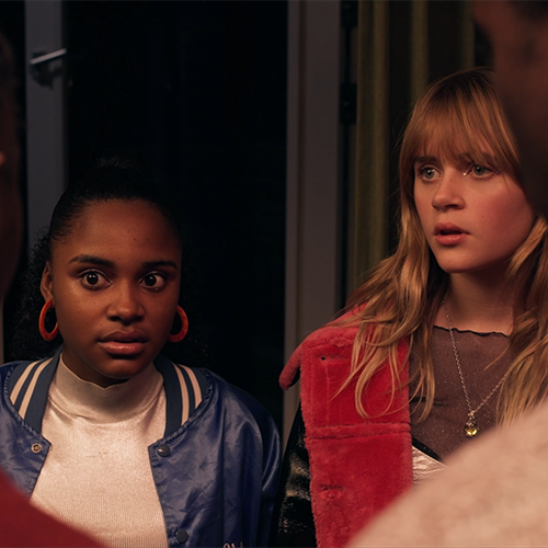 Still from 'Gedrogeerde Ouders?', episode 6 of Broodje Aap. It is an over the shoulder shot of two teenaged girls, one Black and one white, in hip 'going out' clothing. They are looking shocked at the two people we are looking over the shoulder from; two Black adults.