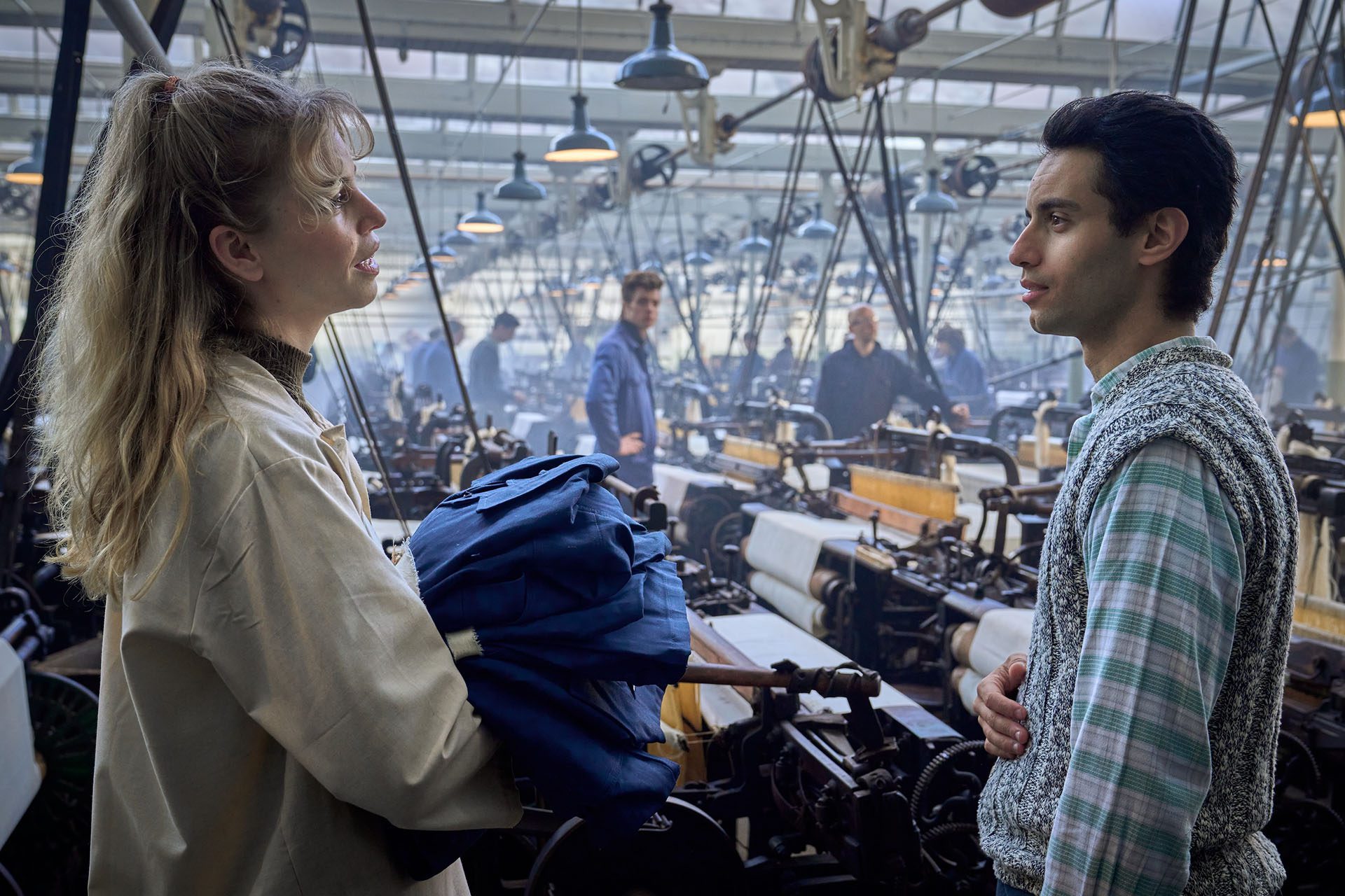 Still from Tegendraads. Johanna and Franceso are looking at each other in the middle of the textile factory workfloor.