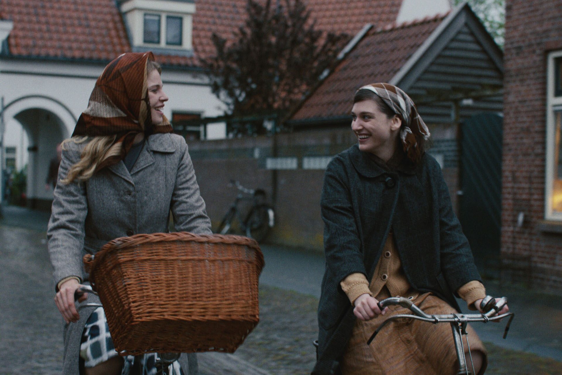 Still from Tegendraads. Johanna and Aleid, two Dutch white women, are on bikes. They both have scarves on their head and are looking at each other.