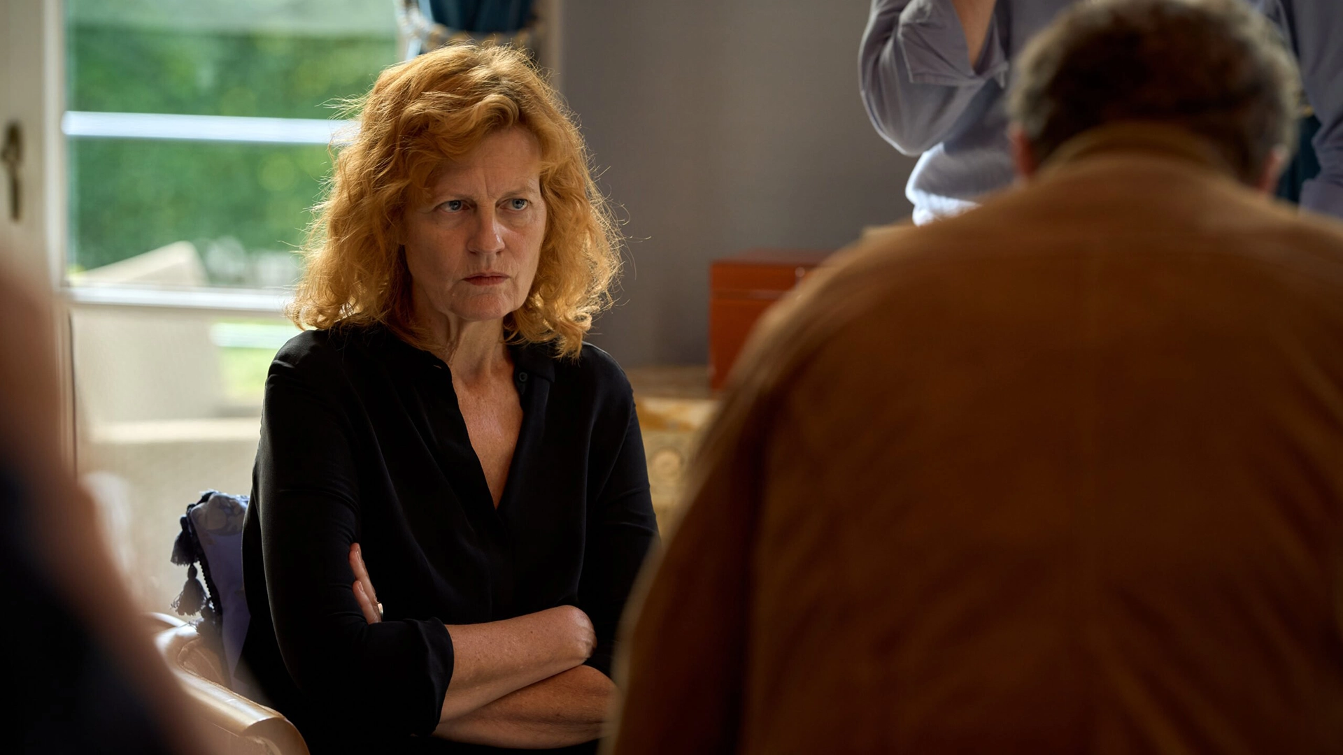 Still from VDV S4E1 Safe in Amsterdam. It's an over-the-shoulder medium shot on Bibi Franken, a 60-or-something white woman with shoulder-length ginger, wavy hair. Her arms are crossed and she looks sternly at the person whose shoulder we're looking over.