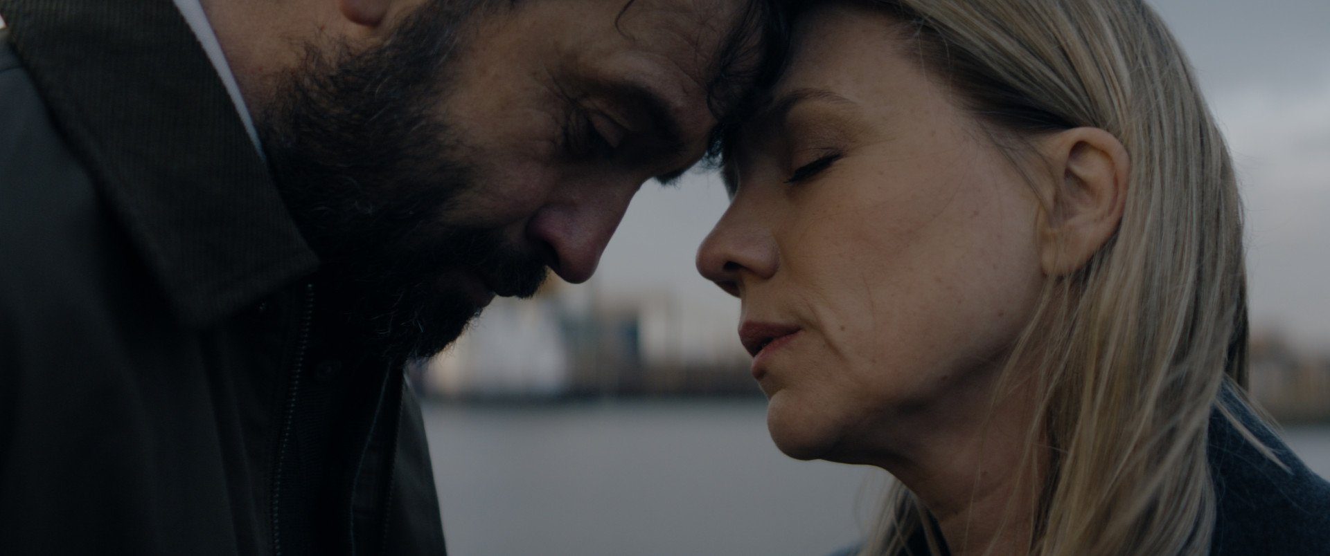 Still from Anoniem S2. A close-up of Jurre (Jeroen Spitzenberger) and Saar (Anniek Pheifer), a white middle-aged woman with half long blonde hair. They are touching their foreheads in an intimate gesture, both eyes are closed.