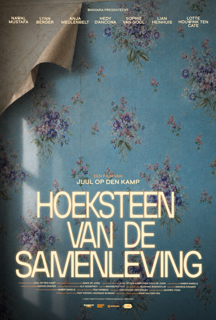 Poster for 'Hoeksteen van de samenleving'. The background is a wall with old-fashioned blue and pink floral wallpaper. But, it's peeling up in the corner, symbolising the breaking down of old patterns and habits. The title of the film is written in a pale yellow near the bottom of the poster.